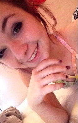 A smiling woman with dark hair and makeup, wearing a colorful top, posing closely with her hand near her face.