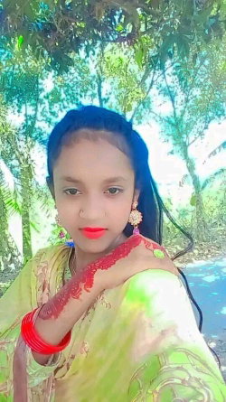 A young woman with dark hair and red lipstick wears a green traditional outfit with henna on her arm, posing outdoors