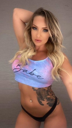 Blonde woman with wavy hair poses in a tie-dye crop top and black thong, showcasing a curvy figure and large side