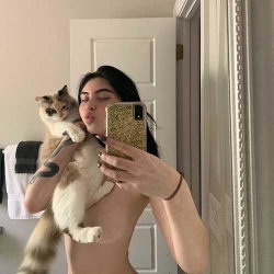 Woman holding a cat, taking a selfie in a bathroom with a white door.