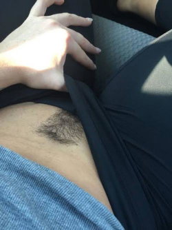 Close-up of a person's lower abdomen with visible pubic hair, wearing black clothing and a blue ribbed top, hand