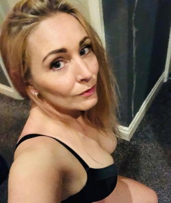 Blonde woman with a curvy figure wearing a black bra, posing indoors in a selfie-style shot.