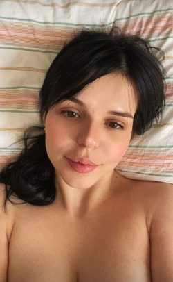 Brunette woman with shoulder-length hair lying on a striped pillow, bare shoulders visible, looking directly at the