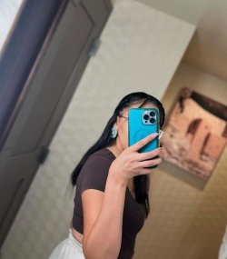 Woman with long dark hair taking a selfie in a bathroom mirror.