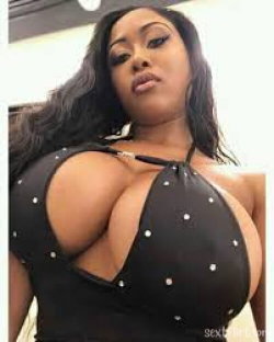 A curvy woman with long dark hair wears a black studded halter top, posing indoors with a confident expression.