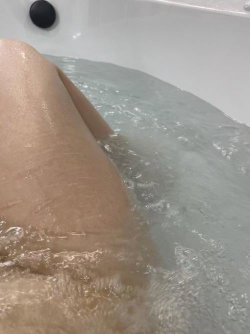 Close-up of a person's leg submerged in bubbly water inside a white bathtub.