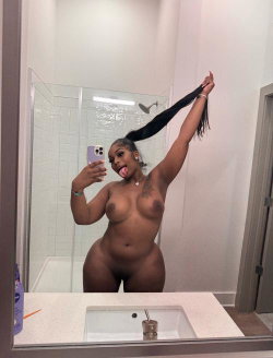 Curvy woman with long dark hair takes a mirror selfie in a bathroom, topless and sticking out her tongue.