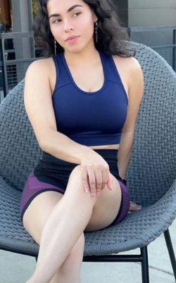 A brunette woman in a blue sports bra and purple shorts sits on a gray chair.