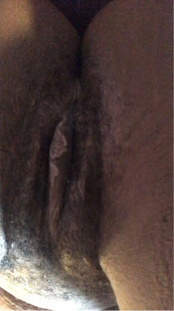 Close-up of a person's lower body, showing bare buttocks and genital area in dim lighting.