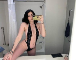 Brunette woman in a black sequined halter one-piece takes a mirror selfie in a bathroom, showing a curvy figure with