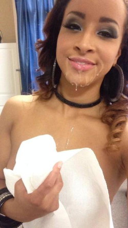A woman with curly hair and dramatic makeup holds a towel over her chest while liquid drips from her mouth, in a