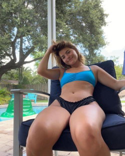 A woman with a curvy body type lounges in a blue bikini by a pool.