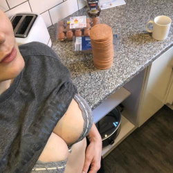 A woman in a gray t-shirt and striped bra stands in a kitchen, partially visible with arm and shoulder showing, near a