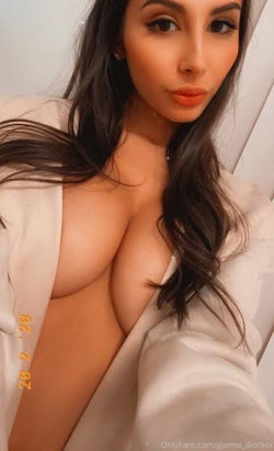 Brunette woman with long dark hair takes a close-up selfie, wearing an open light-colored robe that reveals her bare