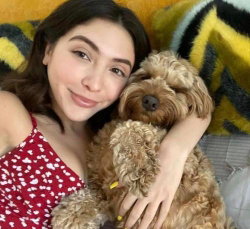 A woman with dark hair in a red polka-dot top hugs a fluffy brown dog on a colorful striped blanket.