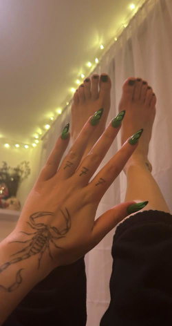 Person with green nail polish, scorpion tattoo on hand, and small finger tattoos, feet visible in cozy room with string