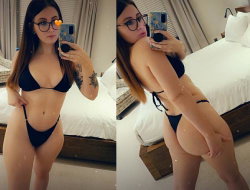 Brunette woman in black bikini takes mirror selfies in a bedroom, showing tattooed arm and curvy figure.