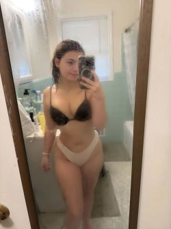 Curvy woman in black lace bra and beige underwear takes mirror selfie in bathroom, hair wet, holding phone.