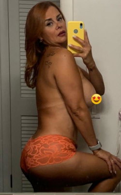 A woman with reddish hair takes a mirror selfie, wearing orange lace underwear, showing her back and side profile in a