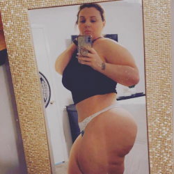 Curvy woman in black crop top and white thong takes mirror selfie, showing full body from front angle.