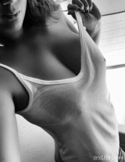 A woman with dark hair in a white tank top pulls the strap down, revealing part of her chest in a close-up
