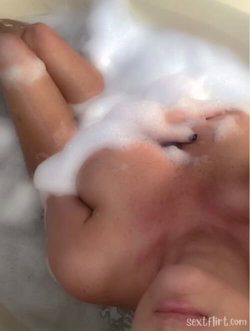 Close-up of feet submerged in soapy bathwater, with bubbles covering toes and skin.