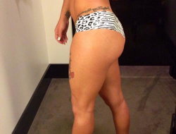 Curvy woman in leopard-print underwear showing back and thighs, with visible tattoos on lower back and leg, standing