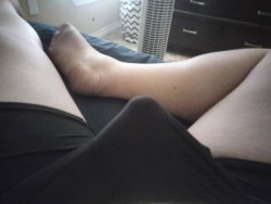 Close-up of a person's legs and feet resting on a bed, wearing black bottoms, in a bedroom setting.