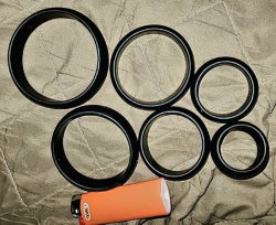 Six black circular rings and an orange lighter arranged on a textured beige fabric surface.