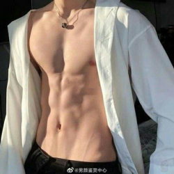 A muscular man with defined abs wearing an open white shirt and black pants, standing indoors with sunlight