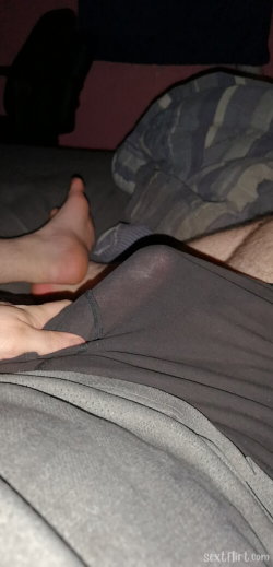 Close-up of a person's lower body in dark clothing, with bare feet visible on a bed or couch, partially covered by