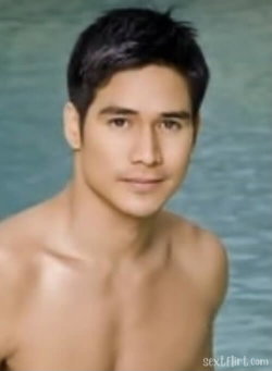 Shirtless man with short dark hair and a lean build, standing against a blurred water background.