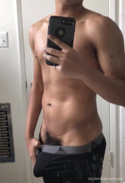 Shirtless muscular man taking a mirror selfie, wearing black Adidas underwear, standing in a bathroom.