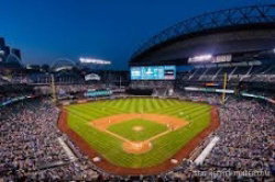 A nighttime baseball stadium filled with spectators, illuminated field under a dark sky with a large scoreboard and