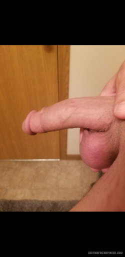 Close-up of a man's erect penis being held, with visible pubic hair and tiled floor in background.