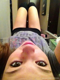 A woman with brown hair lies on her back, looking up at the camera, wearing a patterned top and black socks in a