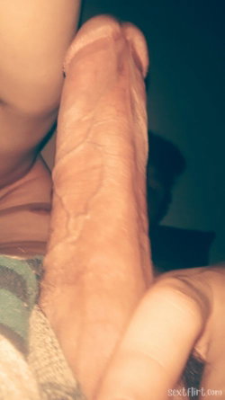Close-up of a penis being held, partially visible skin and fabric in background.