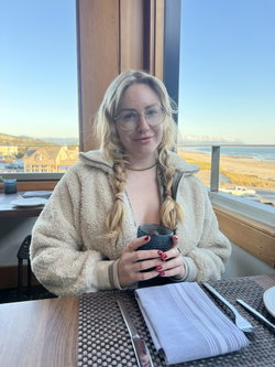 Blonde woman with braided hair and round glasses wears a cozy white fleece jacket while sitting at a restaurant table