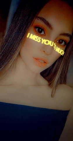 Brunette woman with orange makeup in a dark top, taking a close-up selfie with text overlay.