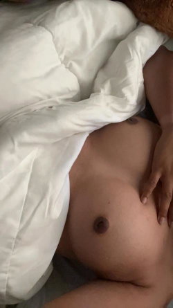 Close-up of a person's bare chest and stomach partially covered by white bedding, hand resting on the torso.