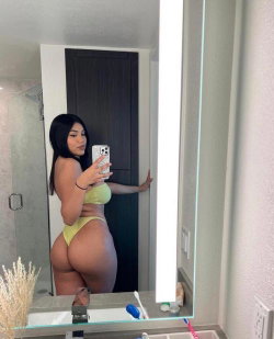 Brunette woman in lime green lingerie takes a mirror selfie in a bathroom, showcasing a curvy figure.