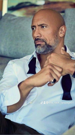 Bald man with a beard adjusts his tie while sitting on a couch.