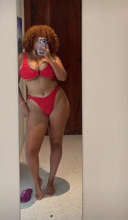 Petite woman in red lace bra and thong posing by a wooden door with a phone in hand