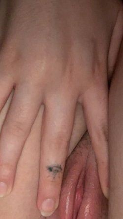 Close-up of a hand with a small tattoo on the finger resting on a wet, exposed genital area.