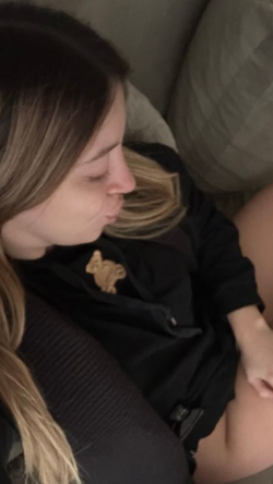 Slim woman with wavy blonde hair lies on gray pillows in open black jacket.