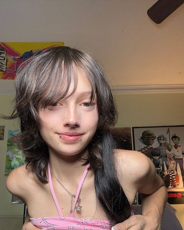 Slim woman with shaggy dark hair, pink spaghetti strap top, in bedroom with posters.