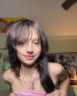 Slim woman with shaggy dark hair, pink spaghetti strap top, in bedroom with posters.