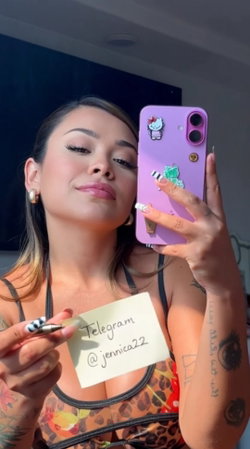 A woman with dark hair and tattoos takes a mirror selfie in a leopard-print top, holding a note with a Telegram handle.