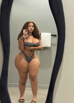 Curvy woman in black and white bikini taking a selfie in a bathroom.