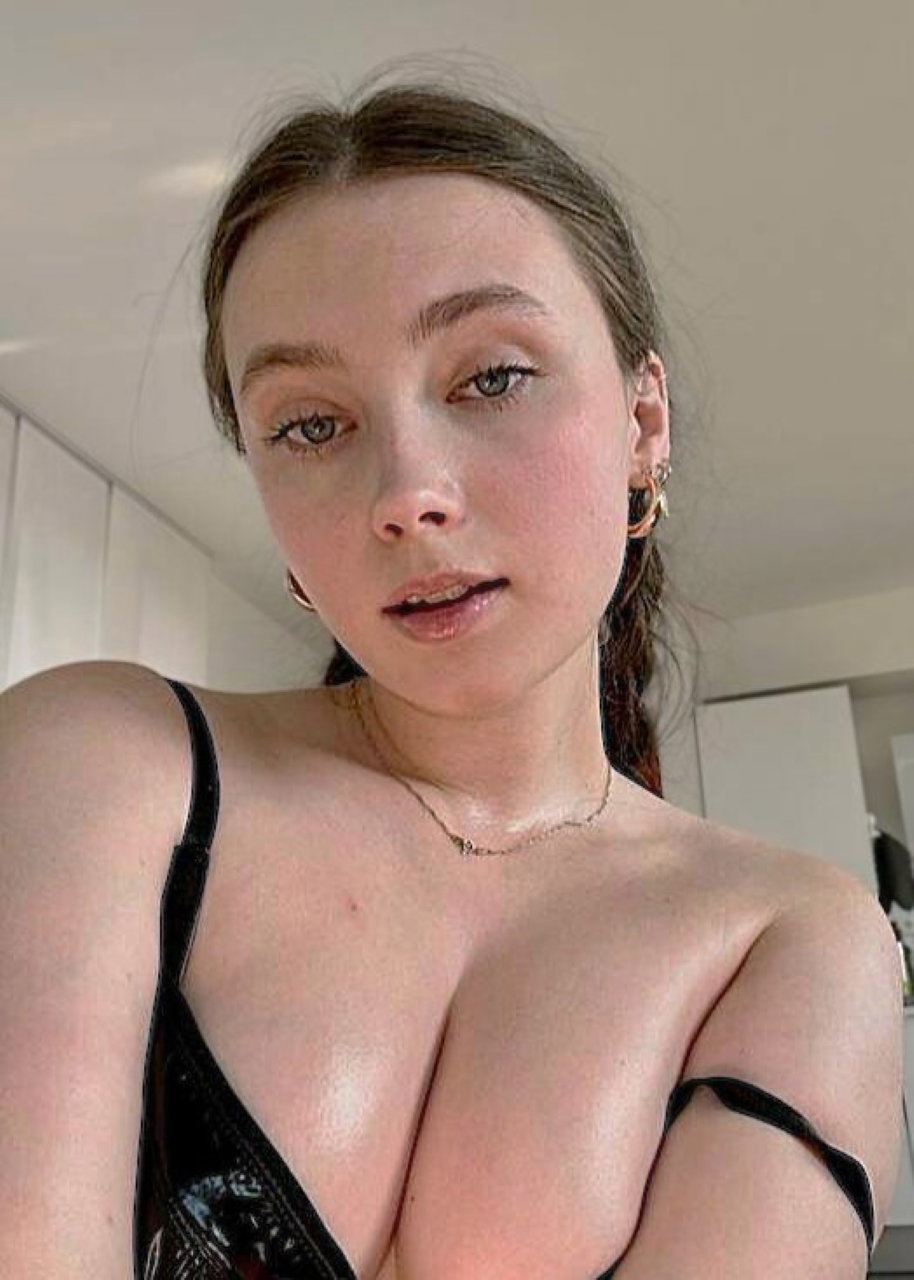 Petite brunette in shiny black strapless top takes selfie in kitchen.